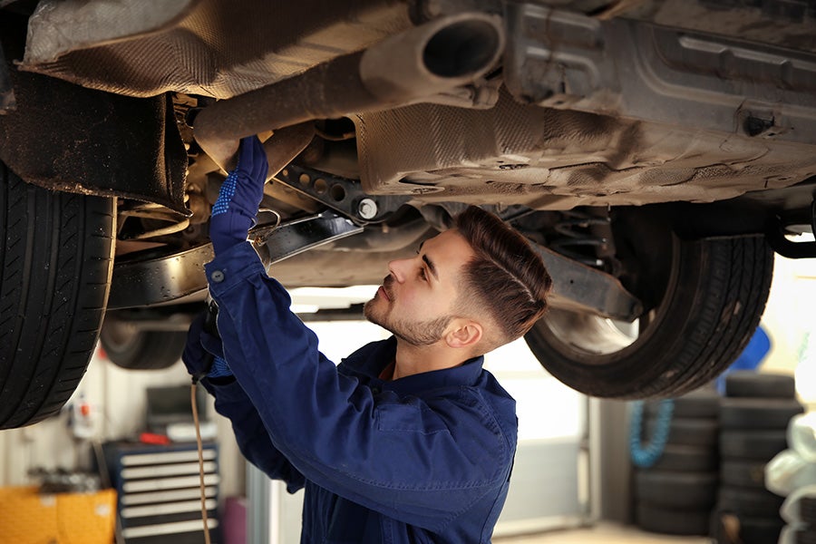 Mechanic in blue coveralls and gloves working on the underside of a car's exhaust system