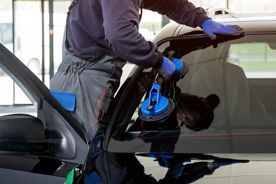 Technician wearing blue gloves uses suction cups to install a new car window on a black vehicle